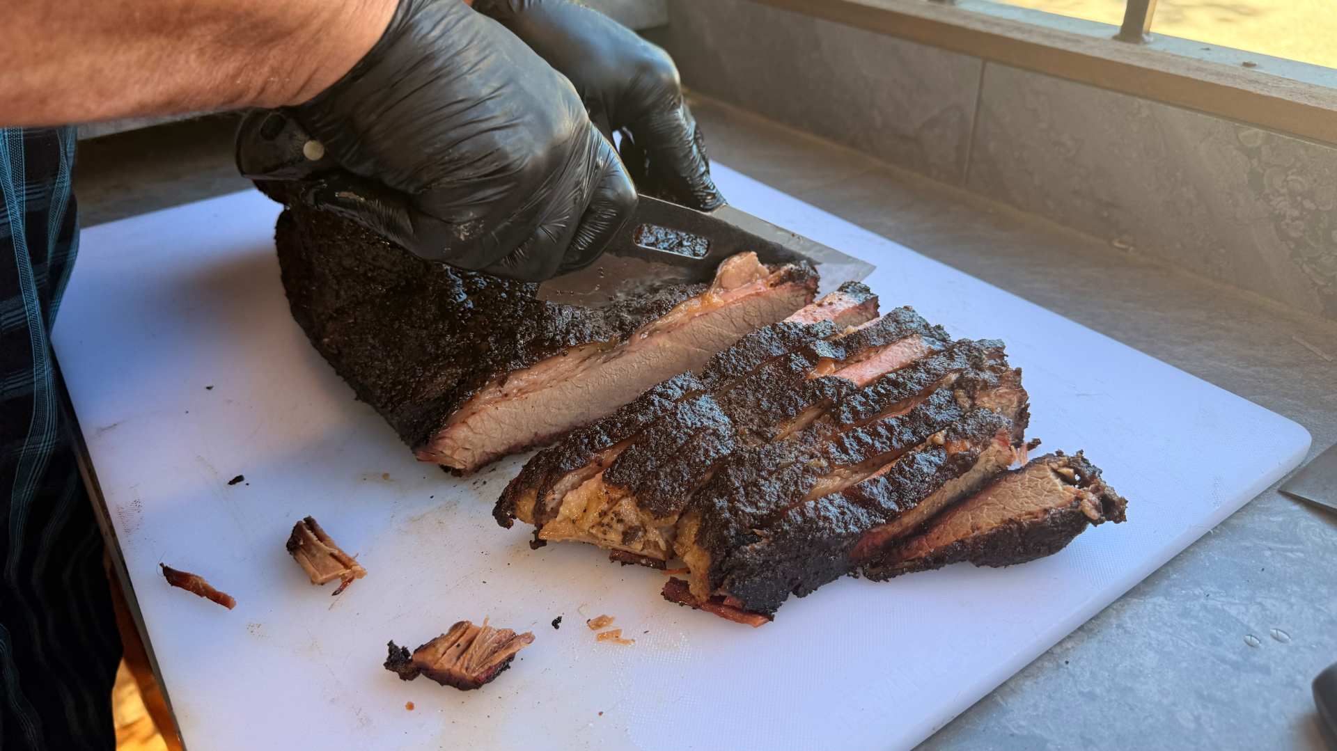 Slicing a smoked Texas brisket with dark peppery bark at the food truck window